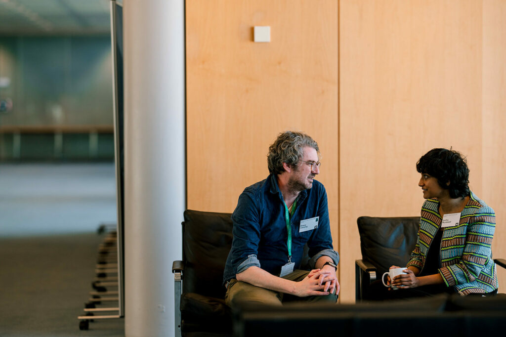 A man and a woman sitting side by side in an office area, having a conversation.
